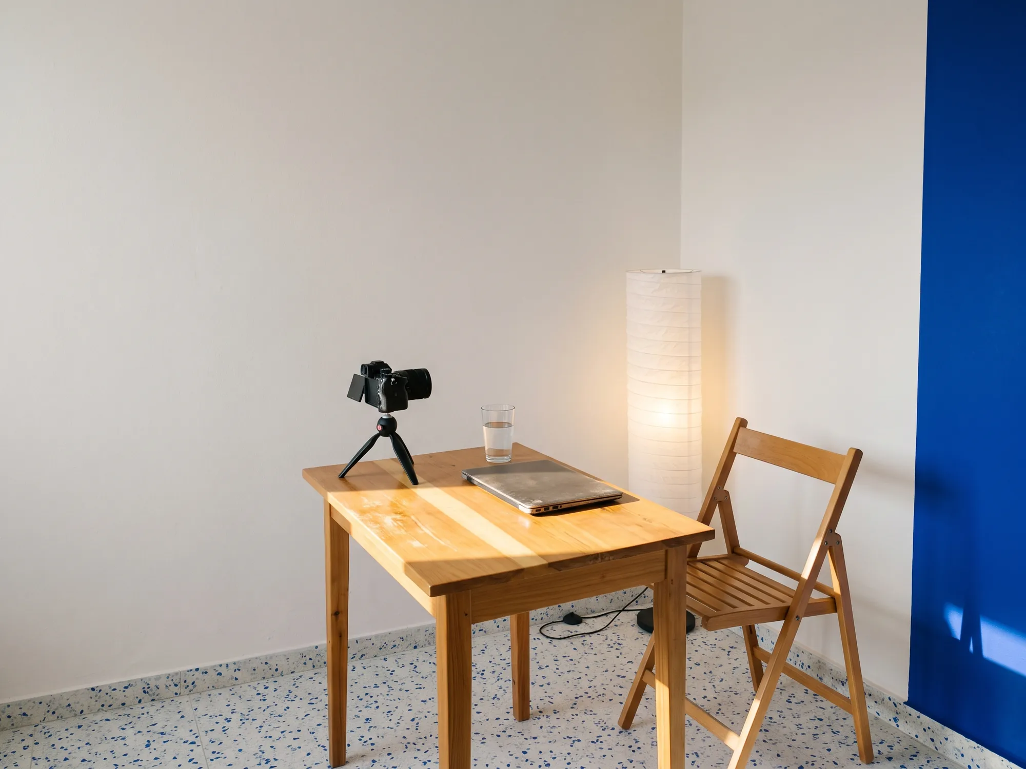 A camera on a small tripod, a laptop and a paper lamp, set up for the online class