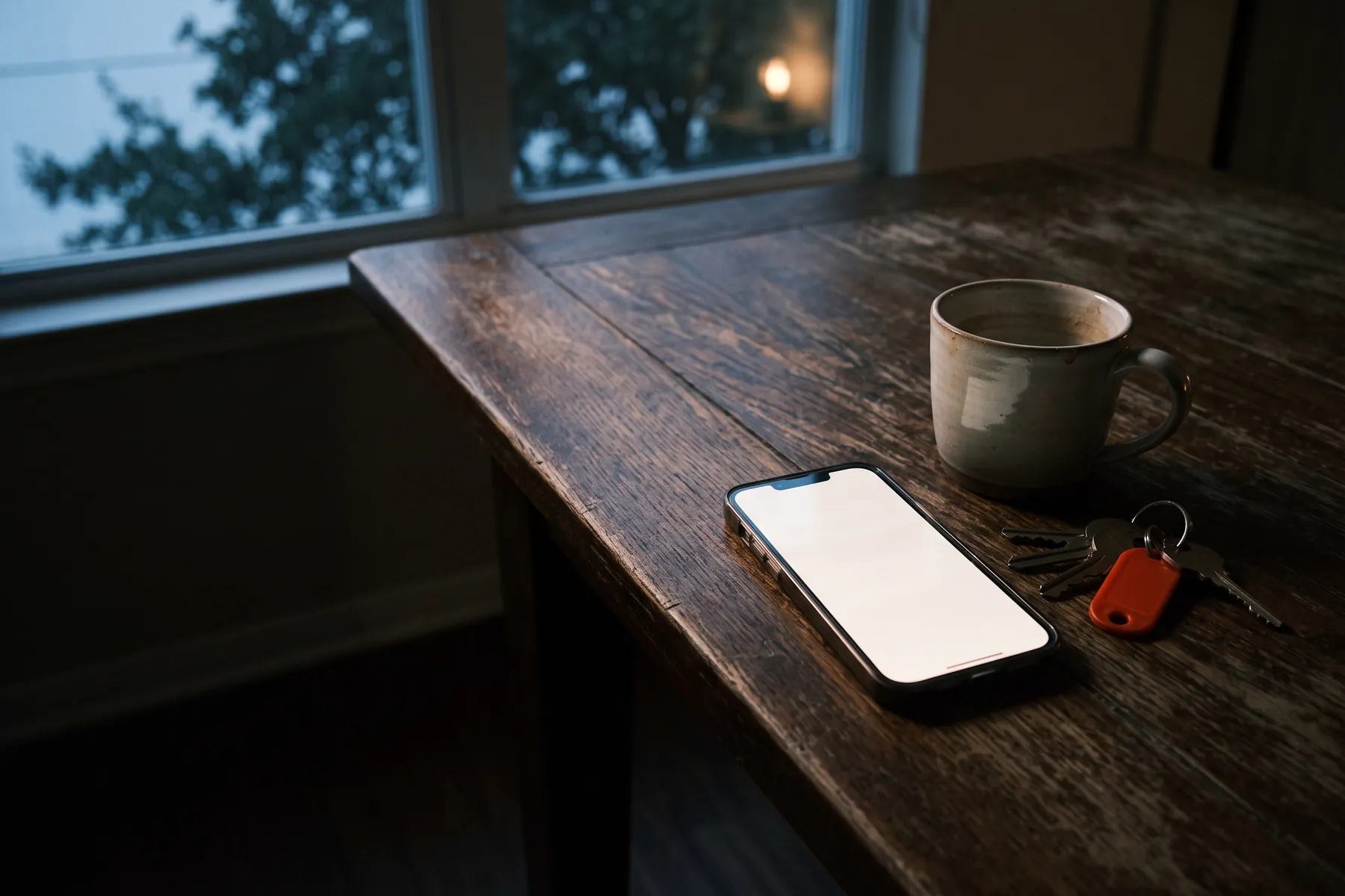 A phone lying face up on a kitchen table before dawn.